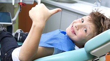 Young boy in dental chair giving thumbs up